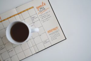 A goal planner showing the month of November sits on a desk. A white mug with black coffee in it sits on the planner.