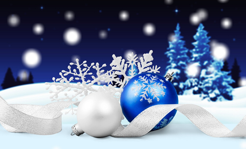 A blue and a white Christmas ornament sit with a white ribbon on a snowlike backdrop, with snowflakes and blue Christmas trees sit in front of a blue stary sky