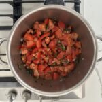 Tomato jam ingredients in a stainless steel pot on a gas stove, ready to simmer