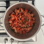 Tomato jam ingredients in a stainless steel pot on a gas stove, simmering
