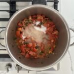 Tomato jam ingredients, with sugar on top, in a stainless steel pot on a gas stove, ready to simmer