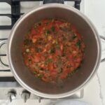 Tomato jam simmering in a stainless steel pot on a gas stove, with liquid reducing, almost ready to bottle