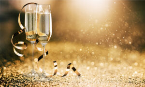 Champagne filled glasses on a gold background with gold ribbons and gold glitter