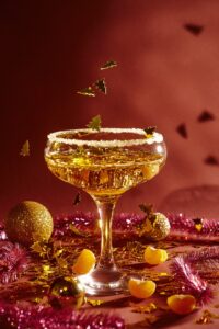 Champagne-filled martini glass sitting on a red background among Christmas fruits and decorations