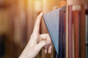 Hand pulling a book from a bookshelf.