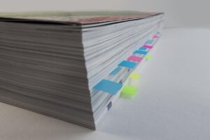 Book sitting on a white table with multi-coloured stickers protruding from the edge of the book to mark pages
