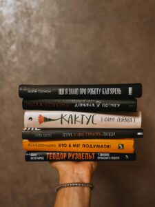 Hand holding aloft five hardcover books sitting on top of each other.