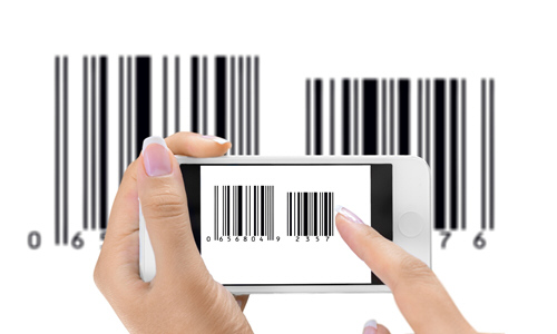Person holding a smartphone and scanning a barcode displayed on the phone screen, with two large printed barcodes visible in the background showing the numbers ‘0618686014’ and ‘076’.