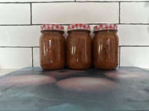 Three jars of tomato jam sitting on a kitchen bench against a white backsplash