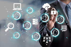 A person in a business suit touches a transparent digital interface displaying floating technology icons, including a magnifying glass, laptop, cloud with a lock, database stack, and connected circular symbols, set against a blurred office background.