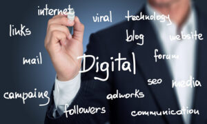 A person in a business suit writes the word “Digital” on a clear surface with a white marker, surrounded by smaller handwritten terms such as “internet,” “viral,” “technology,” “blog,” “website,” “forum,” “seo,” “media,” “communication,” “followers,” “adworks,” “campagne,” “mail,” and “links.”
