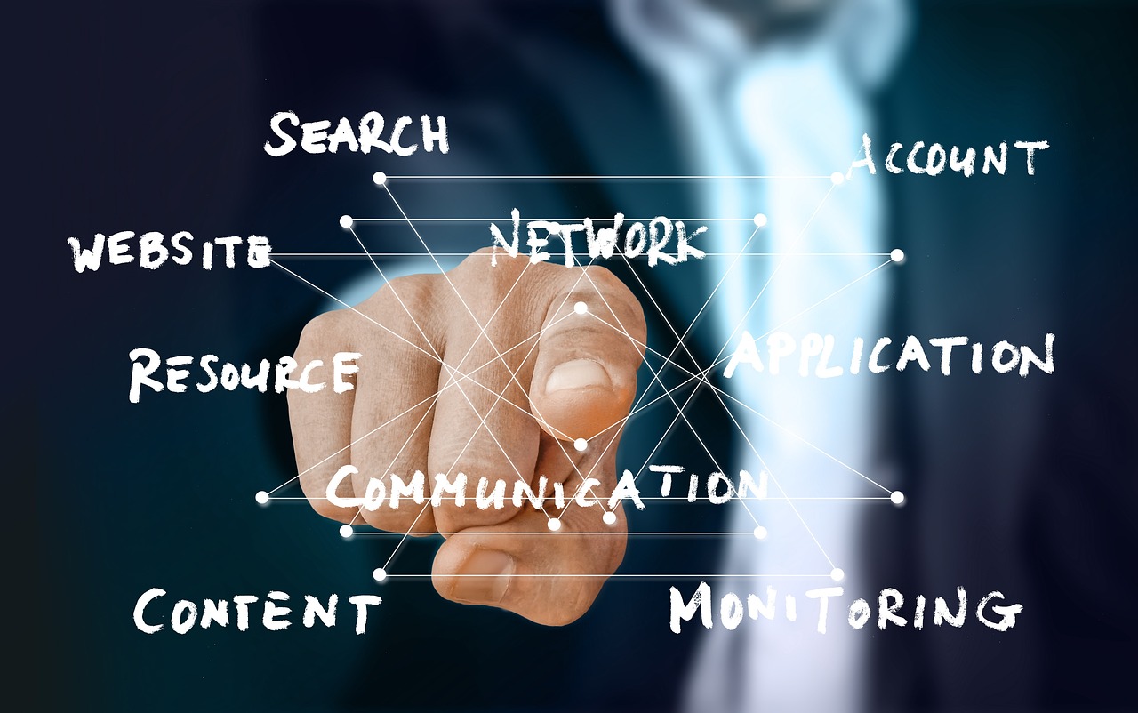 A person in a business suit is pointing forward with their index finger, touching a transparent digital interface. White handwritten-style words—such as “Search,” “Network,” “Application,” “Account,” “Website,” “Resource,” “Content,” “Communication,” and “Monitoring”—are connected by lines and dots, forming a web-like network. The image symbolizes digital connectivity, online communication, and information systems.